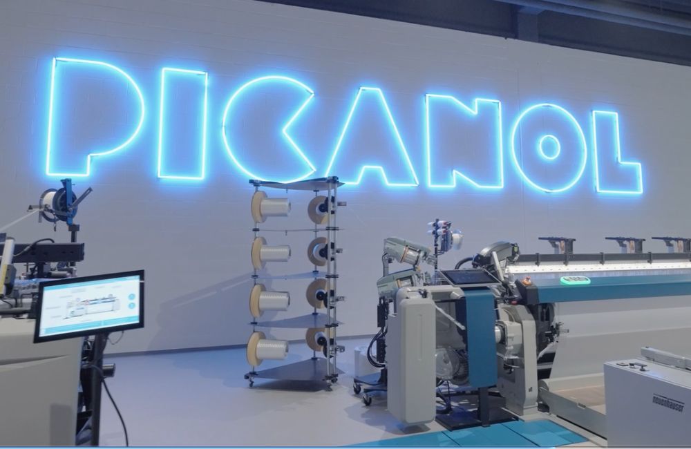 neon Picanol logo on warehouse wall with weaving machines in foreground