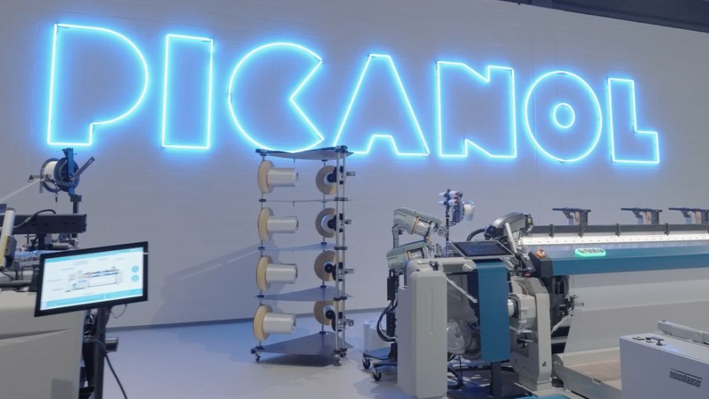 neon Picanol logo on warehouse wall with weaving machines in foreground